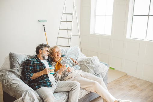 Mature couple painting walls in their apartment, remodeling furniture, and decorating.