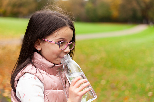 Cute little girl drinking water from a bottle in the autumn park