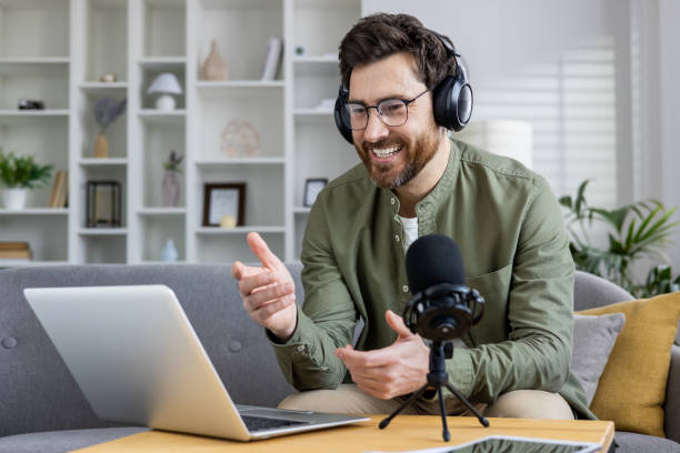 istock Podcast host smiling and talking into microphone during engaging online broadcast from home office 2036021822