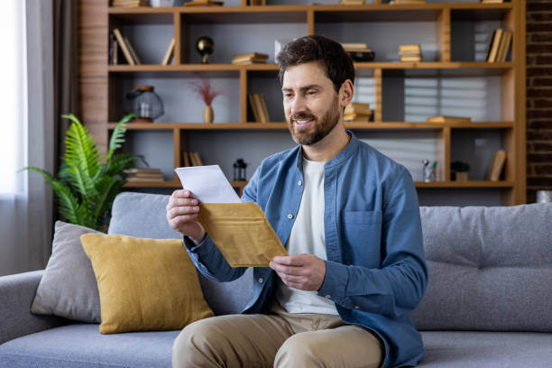 istock Smiling man sitting on couch at home reading a letter with positive emotion 2036023120