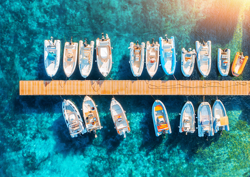 Aerial view of boats and luxure yachts in dock at sunset in summer in Sardinia, Italy. Colorful landscape with sailboats and motorboats in sea bay, jatty, transparent blue sea. Top view. Travel