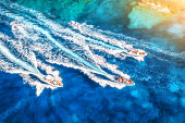 Aerial view of fast floating yachts and boats on blue sea at sunset in summer. Sardinia, Italy. Aerial view of speed boats, sea lagoon, transparent azure water. Top drone view. Tropical seascape