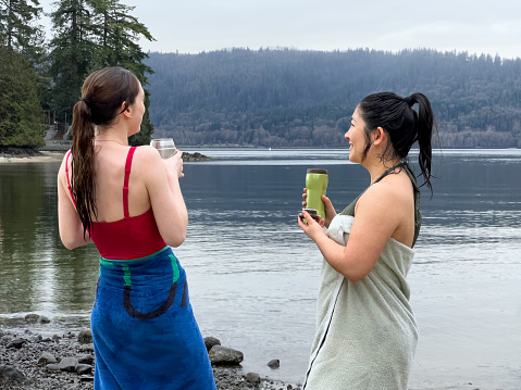Multiracial young women at a local neighborhood public beach drinking hot beverages in reusable thermoses while drying off at after a winter swim in the ocean.  North Vancouver, British Columbia, Canada.