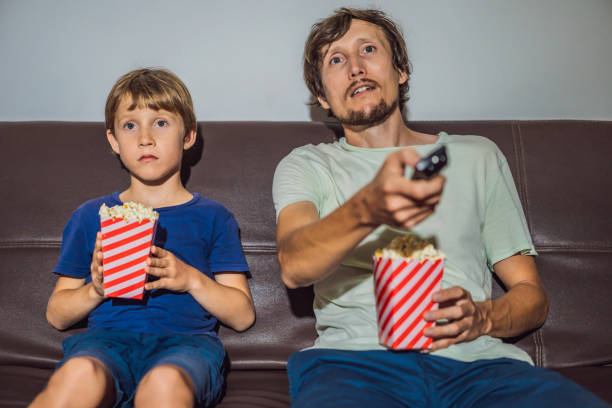 father and son watching tv and eat popcort in evening at home - male men black african descent zdjęcia i obrazy z banku zdjęć