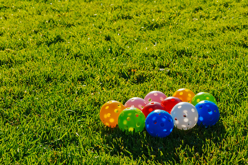 Many light colorful practicing plastic golf balls with holes grouped together at green grass. Practicing golf at home lawn. Close up photo
