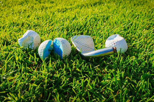 Three broken and damaged golf balls with one broken golf club lay on green grass. close up photo