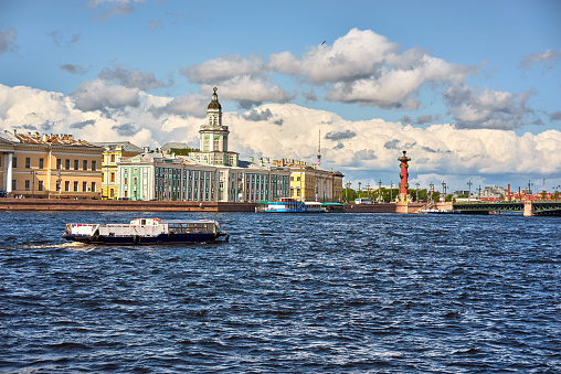 View of the Neva river and Vasilievsky island with old historical buildings. Tourist ship on the river in St. Petersburg, Russia. Blue cloudy sky