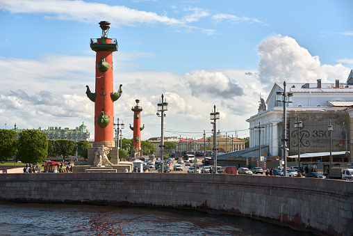 Saint Petersburg. Russia - June 02, 2023: Rostral column (lighthouse) on embankment Neva river. Vasilyevskiy island in Saint Petersburg, blue cloudy sky.