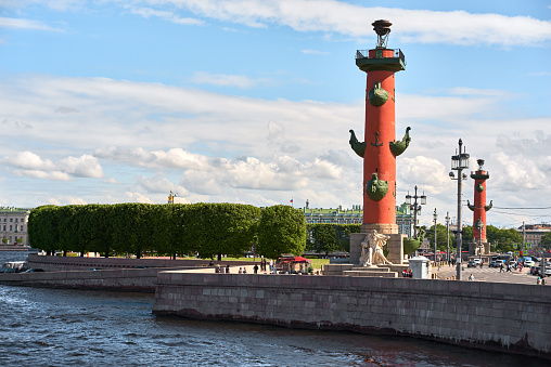 Saint Petersburg. Russia - June 02, 2023: Rostral column (lighthouse) on embankment Neva river. Vasilyevskiy island in Saint Petersburg, blue cloudy sky.