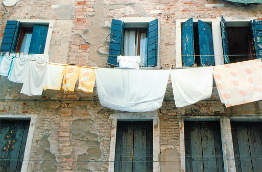 Venice, Veneto, Italy: a moment of everyday life, where various pieces of laundry are hung to dry outside the windows of an aged building with weathered walls and wooden shutters.
