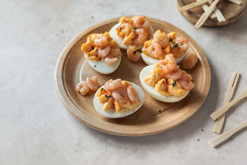 Boiled eggs halved and garnished with cooked shrimps and spices; deviled eggs - cold appetizer close up