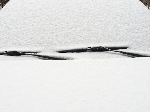 Coating of snow over a windshield with wiper blades. Heavy wet snow covers a vehicle in New England snow country. A winter theme with copy space.