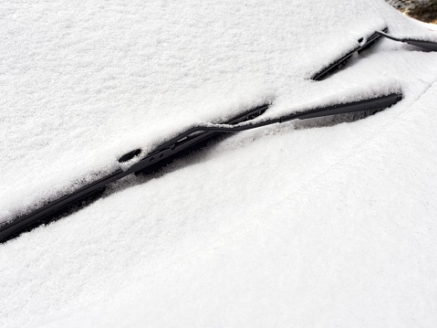 Coating of snow over a windshield with wiper blades. Heavy wet snow covers a vehicle in New England snow country. A winter theme with copy space.
