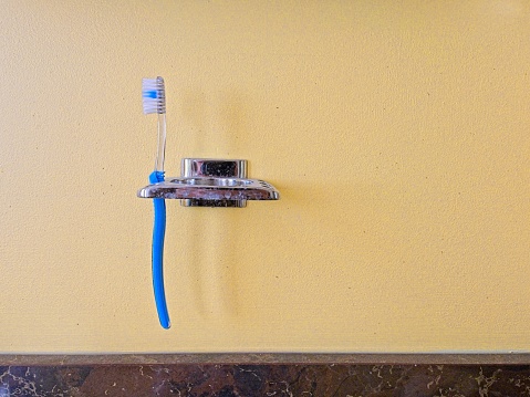 A well worn bathroom wall with toothbrush in brush holder. Hygiene concept with yellow wall and copy space.