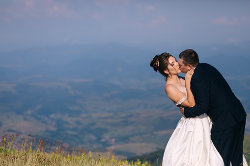 couple in love wedding newlyweds outdoors. the bride in a white dress and the groom in a suit are walking in the summer on the mountain.