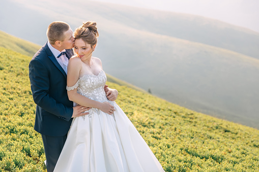 Beautiful wedding couple in the mountains. Stylish groom kisses the bride.