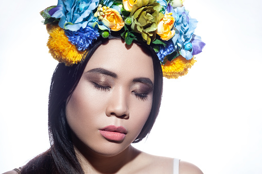 Portrait of beautiful young adult woman with makeup and with a floral ornament in her hair, posing with closed eyes, has calm expression. Indoor studio shot isolated on gray background.
