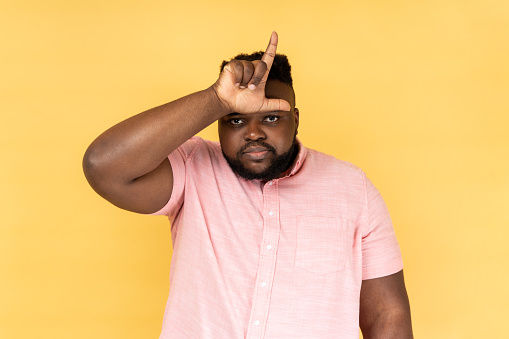 Portrait of upset disappointed man wearing pink shirt showing looser gesture with hand on forehead, having financial and business problems. Indoor studio shot isolated on yellow background.
