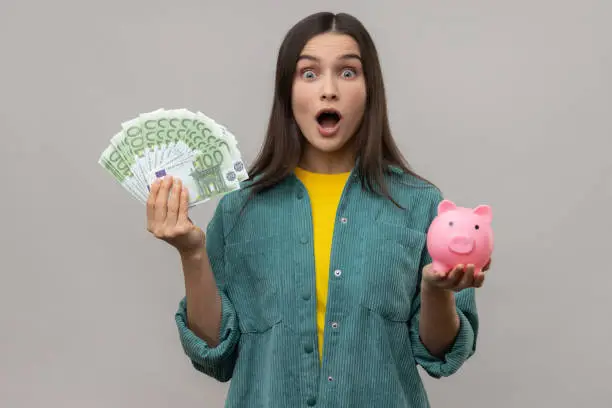 Photo of Shocked amazed woman holding big sum of euro banknotes and piggy bank, profitable investment.