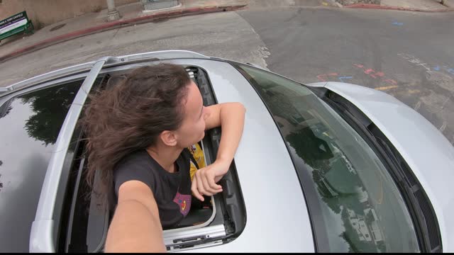 Young excited joyful woman outside on the sunroof of a SUV enjoying the driving on the streets of LA