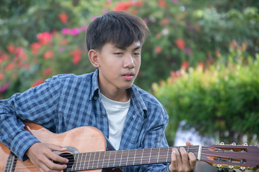 Asian boy spending his freetimes afterschool and on weekend by practising and playing acoustic guitar or ukulele in the backyard of his house.