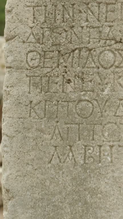 Vertical video. A young female tourist touches ancient stone columns with Greek inscriptions carved on them. Close-up.