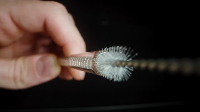 A man cleans a glass drinking straw using a small brush, inserting it inside. Macro shot.