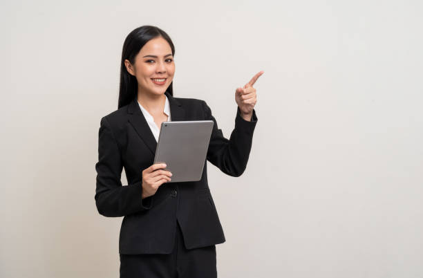 istock Attractive elegant young asian business woman using digital tablet standing on isolated background. Happy young latin female formal black suit holding tablet gadget working service with customer 2036806898