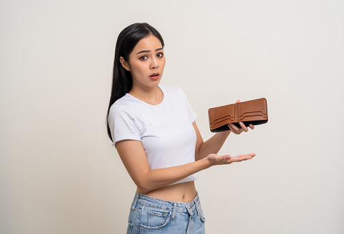Asian business woman looking at empty wallet. Flip it over but don't have money inside wallet. Standing on isolated white background. Poor attractive female on money