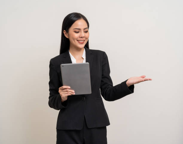 istock Attractive elegant young asian business woman using digital tablet standing on isolated background. Happy young latin female formal black suit holding tablet gadget working service with customer 2036815908