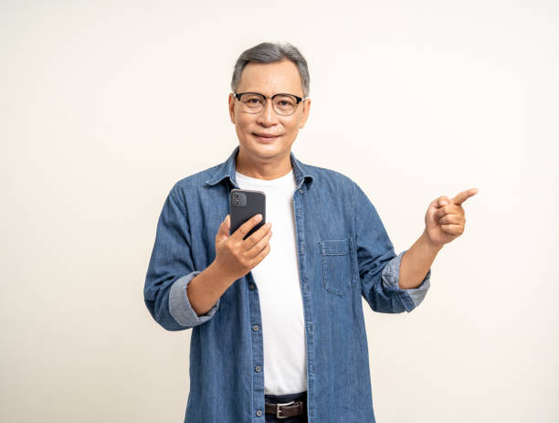 istock Handsome asian mature old man using smartphone palm up  pointing hand on copy space isolated white background. Portrait of cheerful smiling senior asian man holding cell phone. Mature People and lifestyle 2036834453
