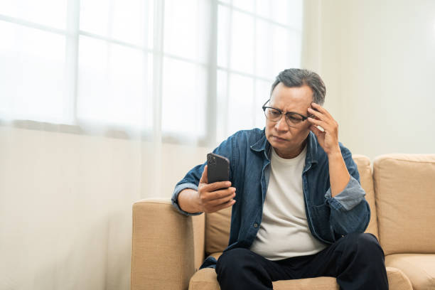 istock Depressed Asian mature old man using smartphone serious thinking on sofa in living room. Portrait stress of senior asian man holding cell phone. Mature People and lifestyle 2036840614