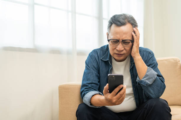 istock Depressed Asian mature old man using smartphone serious thinking on sofa in living room. Portrait stress of senior asian man holding cell phone. Mature People and lifestyle 2036847318