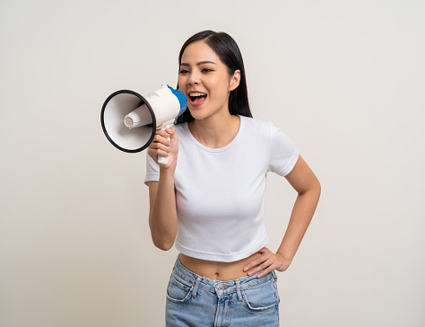 Shout out loud with megaphone. Young beautiful asian woman  announces with a voice about promotions and advertisements for products at a discounted price. Standing on isolated white background.