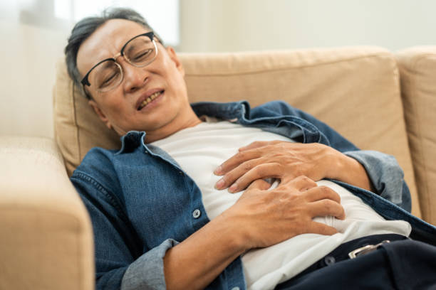 old man senior had a stomach ache and gastritis. mature man put hand on his stomach and squeezed it to relax and soothe has go to toilet need to poop. sitting on sofa in living room at home - old senior adult women tired ストックフォトと画像