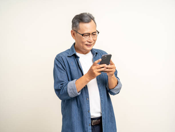 istock Handsome asian mature old man standing using smartphone on isolated white background. Happy Portrait of cheerful smiling senior asian man holding cell phone. Mature People and lifestyle 2036862787