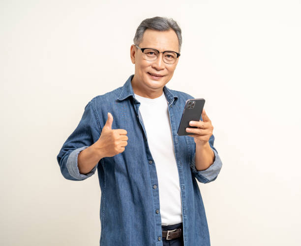 istock Handsome asian mature old man standing using smartphone on isolated white background. Happy Portrait of cheerful smiling senior asian man holding cell phone. Mature People and lifestyle 2036868905