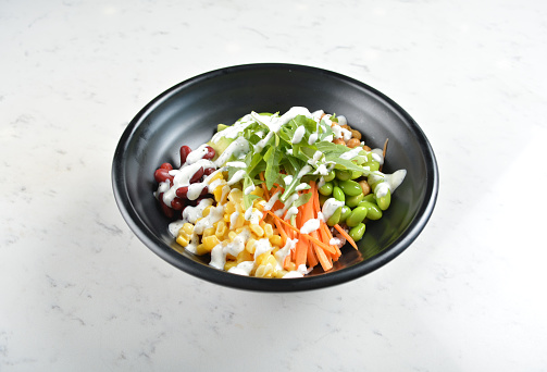 colourful western healthy bowl assorted salad, vegetables, avocado, corn, bean, carrot and salad dressing sauce in white marble table asian cafe healthy poke bowl halal vegan menu