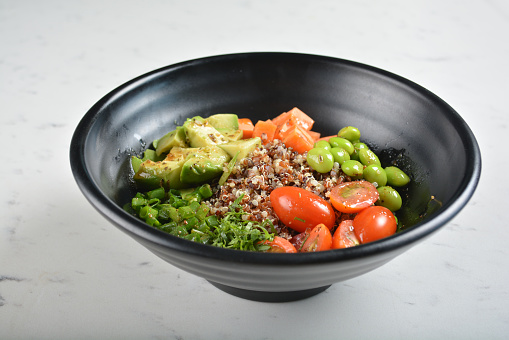 western trio quinoa grain salad bowl with avocado, tomato, pea bean, carrot and brown rice in black bowl in white marble table asian cafe healthy poke bowl halal vegan menu
