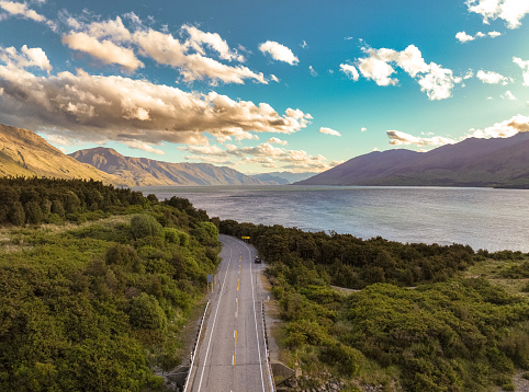 Experience breathtaking aerial views of a country road at Lake Wanaka in South Island, New Zealand. Discover a serene oasis surrounded by majestic mountains and lush green scenery.