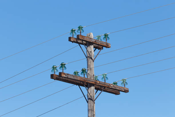 Old wooden electric pole with wires and glass insulators against a blue sky