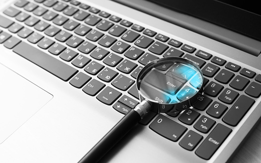 A magnifying glass on a laptop keyboard with a blue reflection in the glass. Information search concept