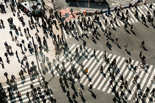 People crossing the road at Shibuya crossing in Japan. Japanese text on road sign means Shibuya station and scramble crossing.