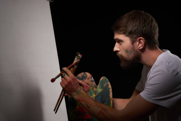 a man with a palette in his hands brush easel art creative approach hobby dark background - 11902 stock-fotos und bilder