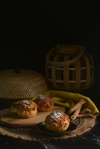 luxury home made chilled vanilla cream puff pastry choux with sugar powder on wood plate and cloth in black background and bamboo basket prop dessert halal menu for cafe