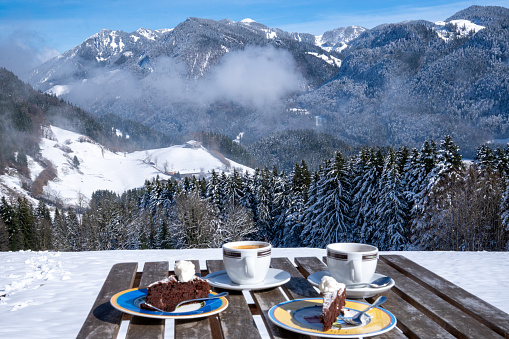 View over a set table with coffee and cake to the Chiemgau Alps and Geigelstein (1808 m), Bavaria, Germany in winter.