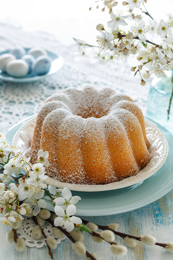 Easter bundt cake, Babka sprinkled with icing sugar on a festive table decorated with spring flowers, close up view