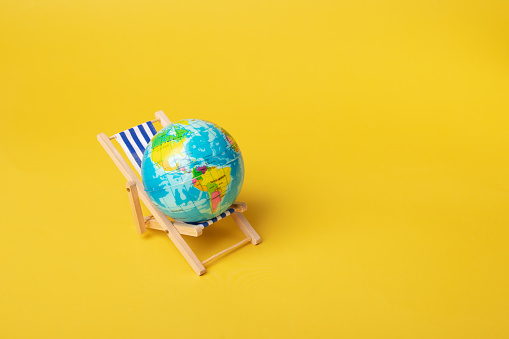 Deckchair with Earth, summer travel concept, globe-trotting ideas, beach vacation, yellow background