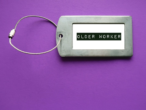 Luggage ID tag on purple background with text written OLDER WORKER, trend of businesses hire more older people, senior employees work longer in rapidly aging society