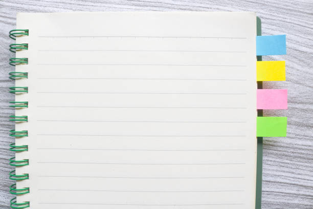 Colorful sticky notes between books. Colorful sticky note bookmarks are attached to the notebook. Bookmarks in a book on wooden table
